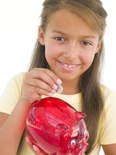 Young girl putting coin into piggy bank smiling